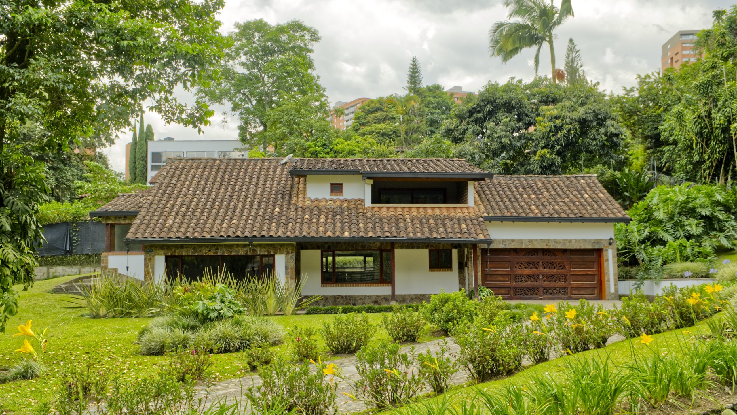 Casa campestre de dos pisos con techo de teja, amplias zonas verdes y jardín rodeado de árboles.